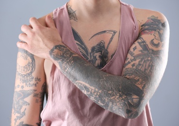 Photo of Young man with stylish tattoos on grey background, closeup