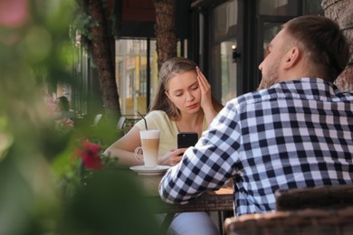 Photo of Young woman distracting herself with smartphone during boring date in outdoor cafe