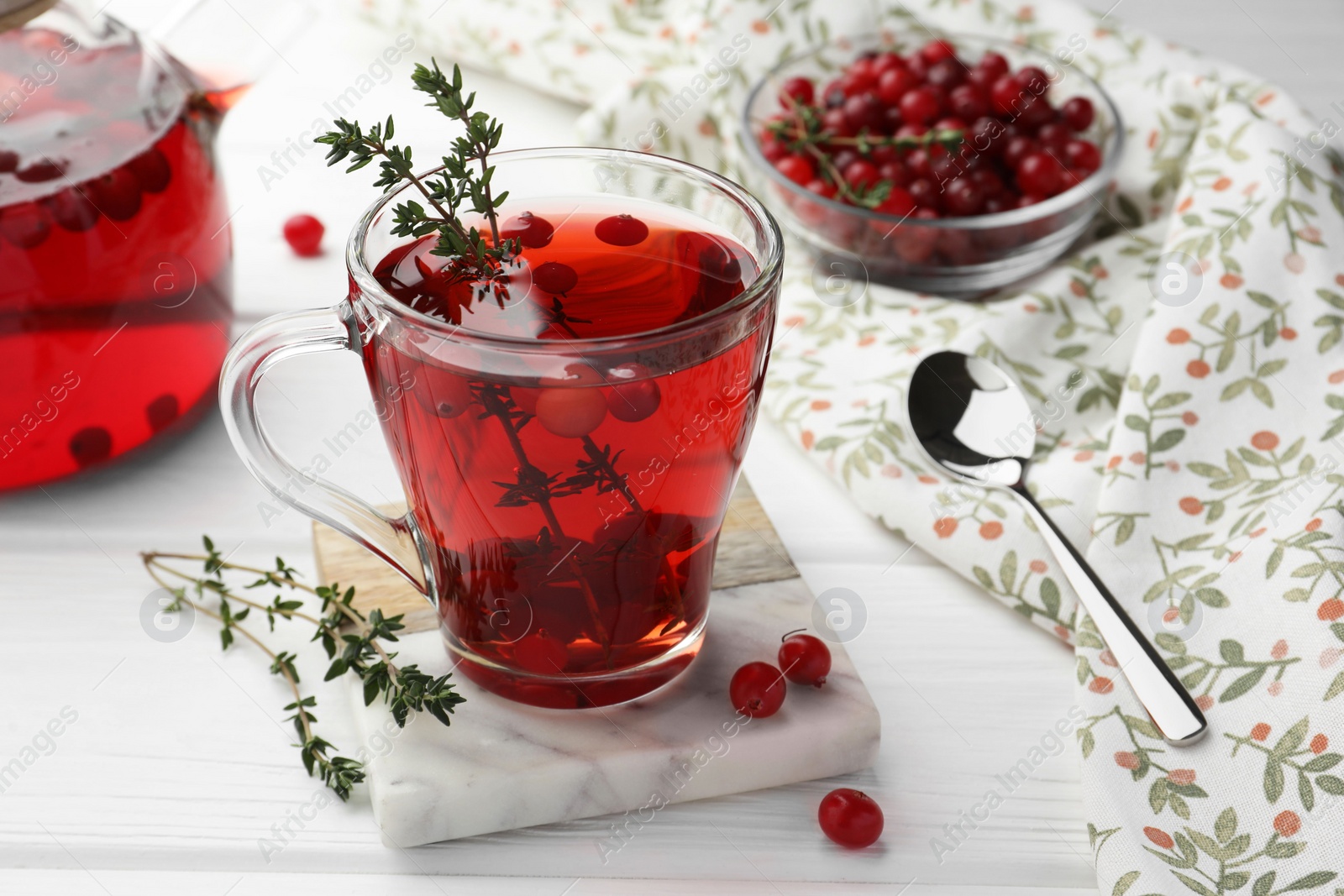 Photo of Tasty hot cranberry tea with thyme and fresh berries in glass cup on white wooden table