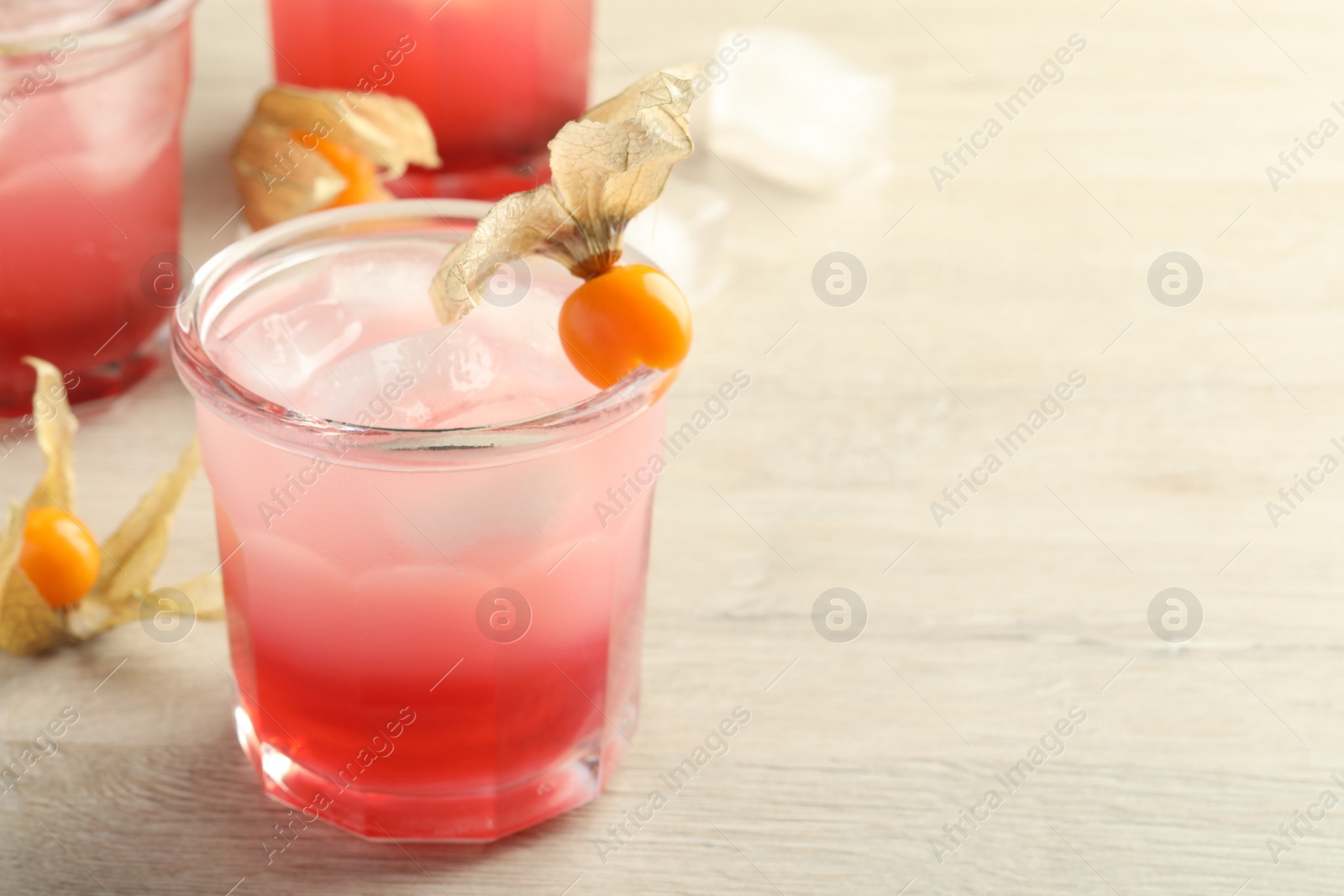 Photo of Refreshing cocktail decorated with physalis fruits on wooden table. Space for text