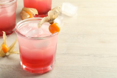 Photo of Refreshing cocktail decorated with physalis fruits on wooden table. Space for text