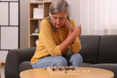 Thoughtful senior woman playing checkers at home
