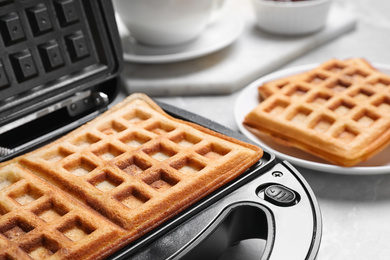 Photo of Modern iron with tasty Belgian waffles on table, closeup