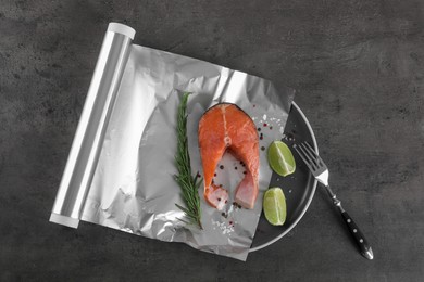 Aluminum foil with raw fish, lime, rosemary and spices on grey textured table, flat lay. Baking salmon