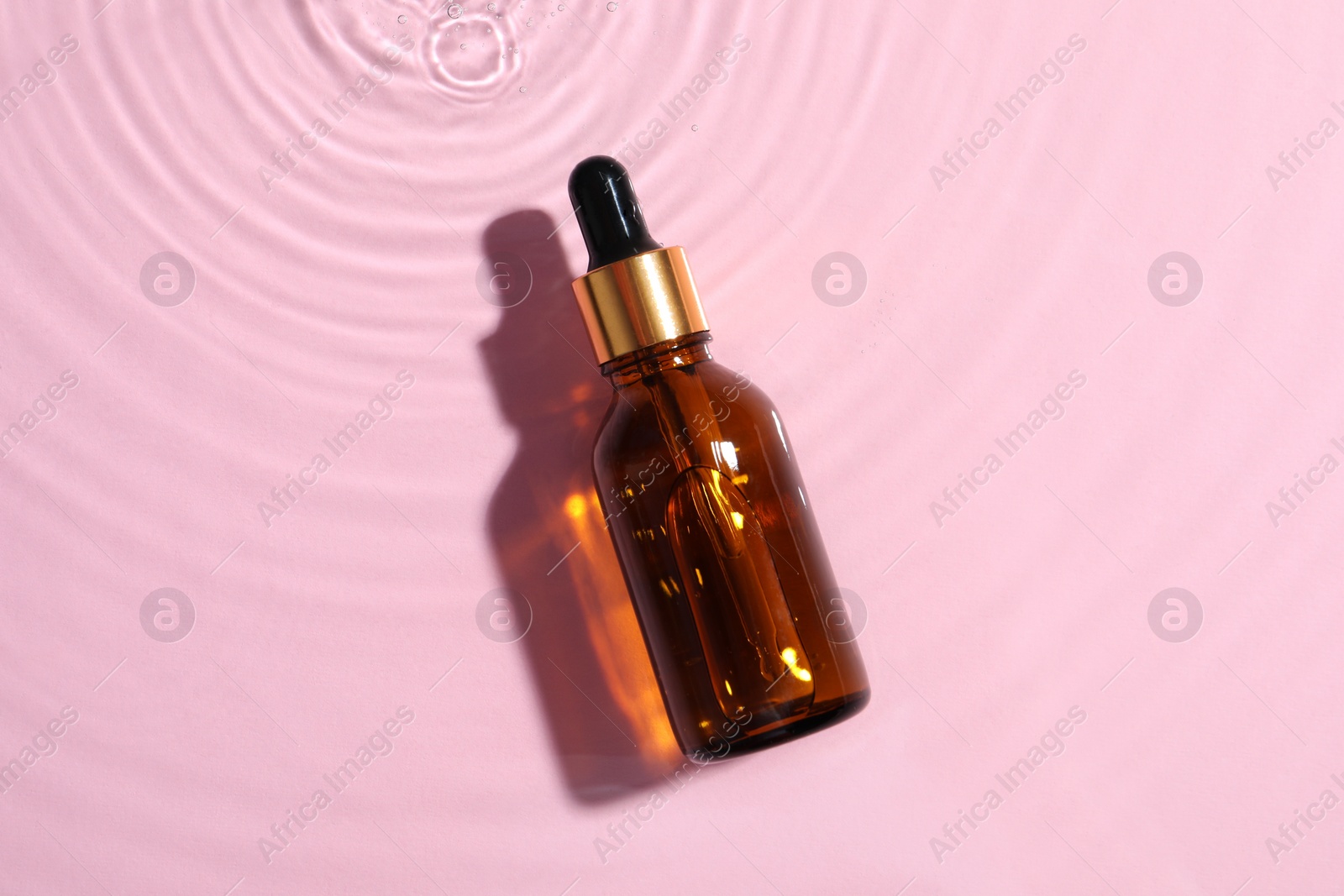 Photo of Bottle of cosmetic oil in water on pink background, top view