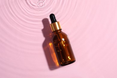 Bottle of cosmetic oil in water on pink background, top view