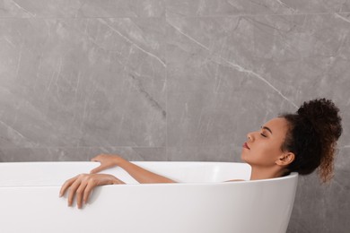Beautiful African American woman taking bath indoors, space for text