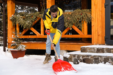 Man removing snow from house yard with shovel on winter day