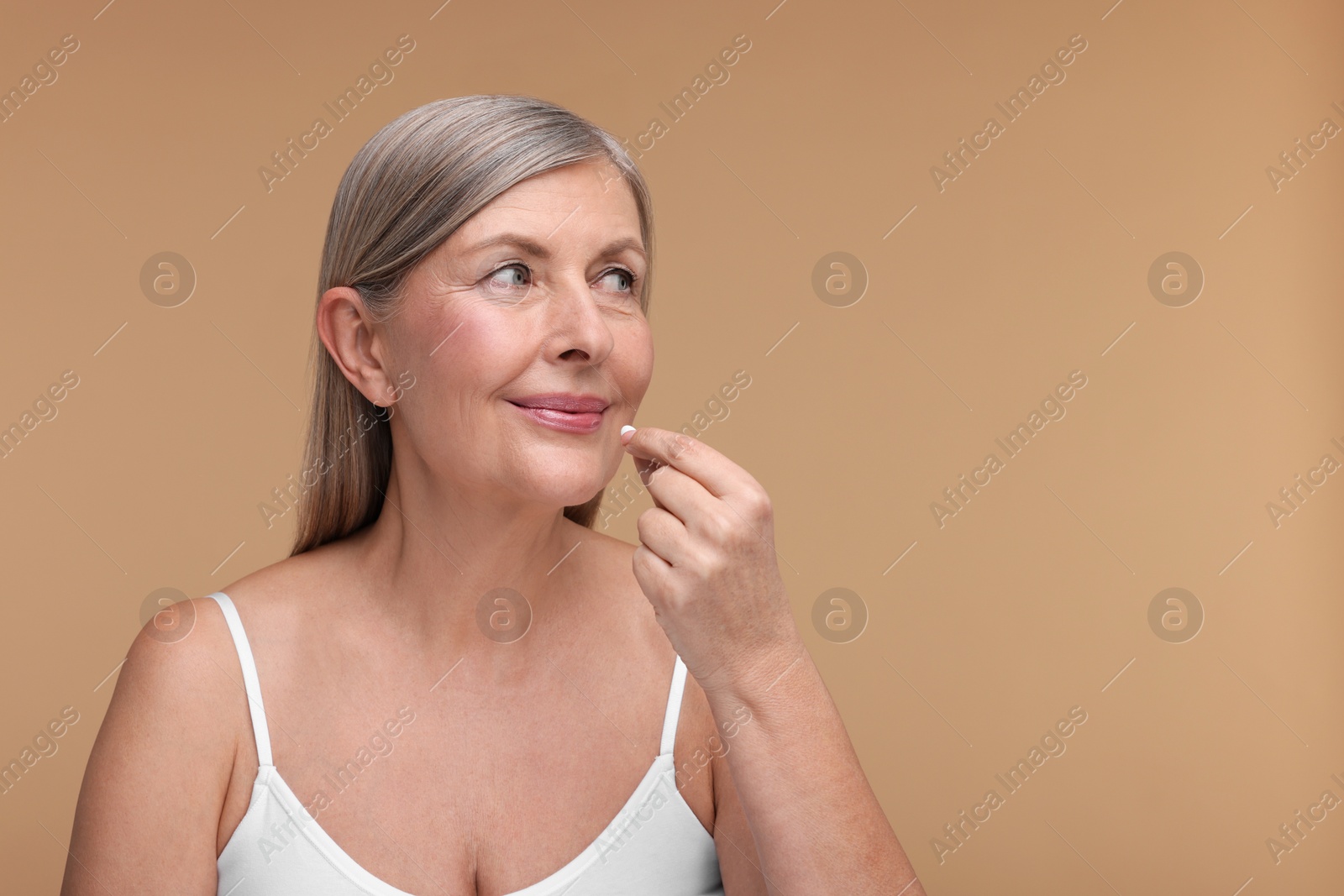 Photo of Beautiful woman taking vitamin pill on beige background, space for text