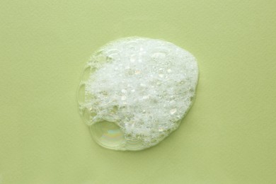 Drop of bath foam on light green background, top view