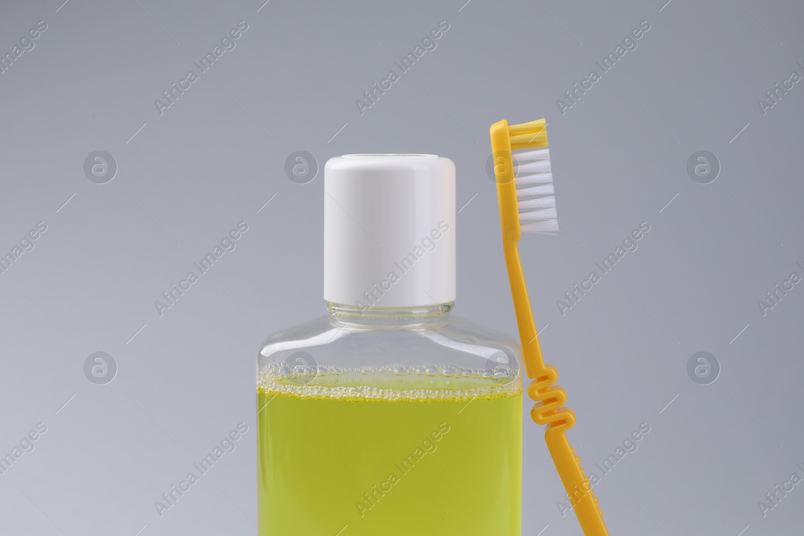 Photo of Fresh mouthwash in bottle and toothbrush on grey background, closeup