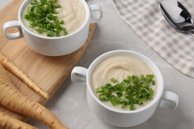 Photo of Bowls with tasty creamy soup of parsnip served on light grey table, closeup