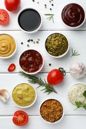 Many different sauces, spices and vegetables on white wooden table, flat lay