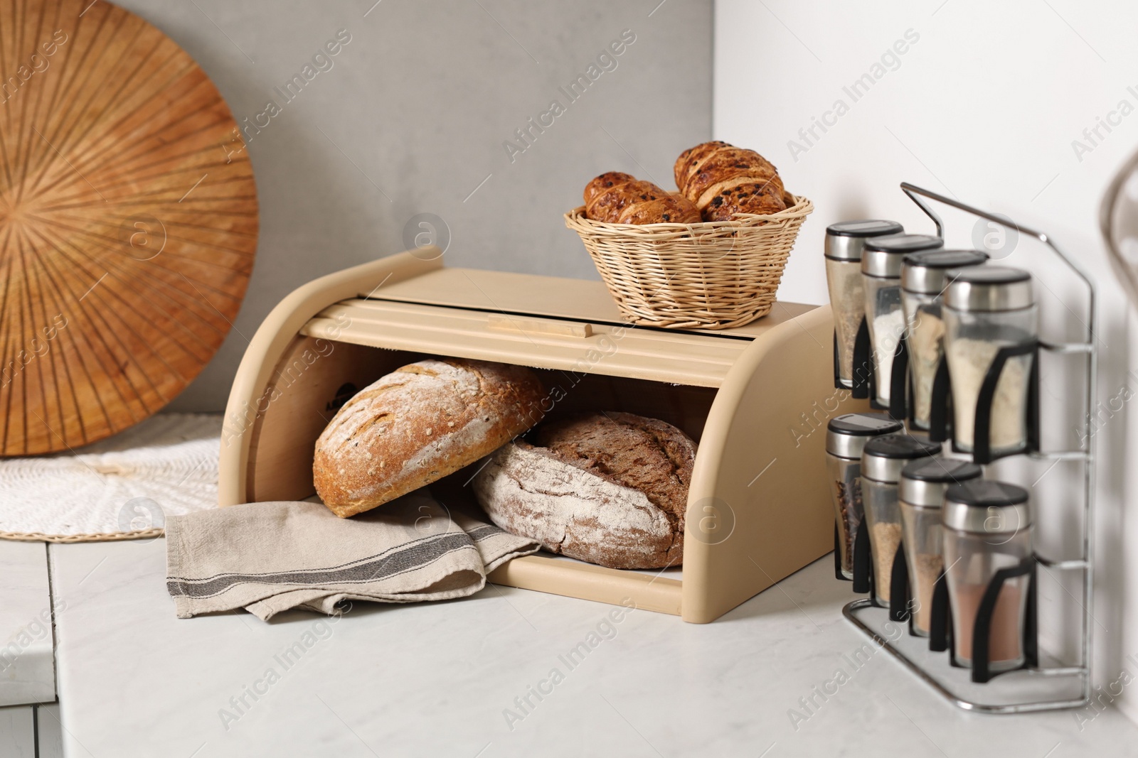 Photo of Wooden bread basket, freshly baked loaves and croissants on white marble table in kitchen