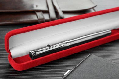 Photo of Case with stylish silver fountain pen and leather notebook on black wooden table, closeup