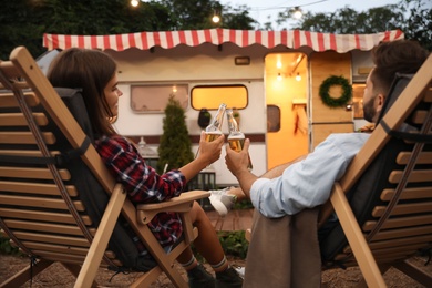 Photo of Young couple toasting with bottles of beer near trailer. Camping season