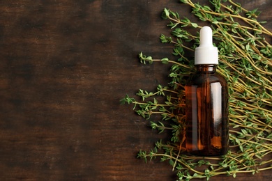 Photo of Bottle with thyme essential oil and fresh herb on wooden background