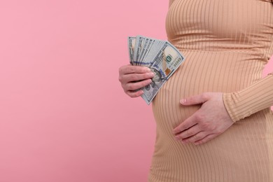 Surrogate mother. Pregnant woman with dollar banknotes on pink background, closeup. Space for text