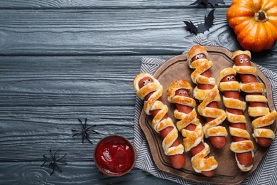 Photo of Cute sausage mummies served on wooden table, flat lay with space for text. Halloween party food