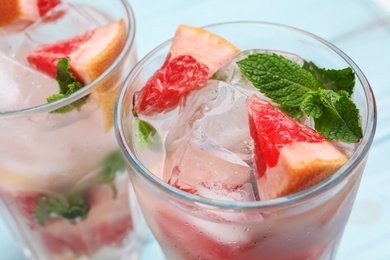 Glasses of grapefruit refreshing drink with ice cubes and mint on table, closeup