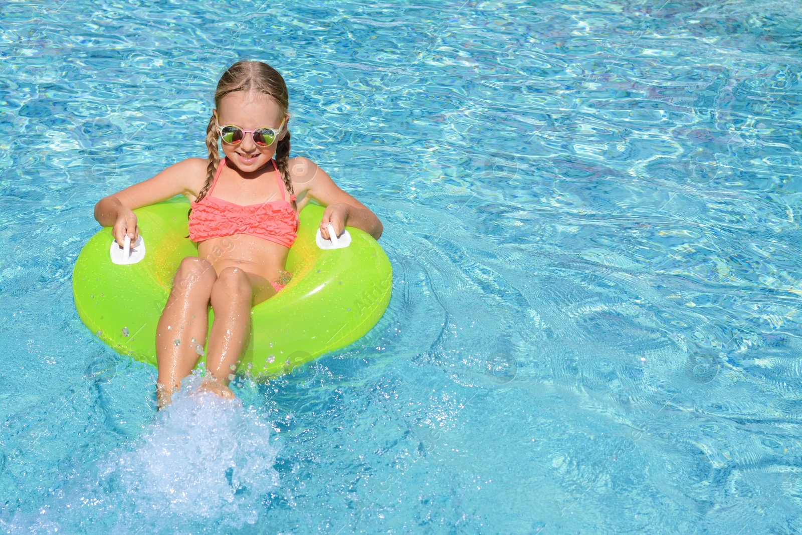 Photo of Cute little girl with inflatable ring in pool on sunny day. space for text