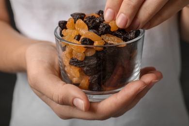 Photo of Woman holding glass with raisins on black background, closeup