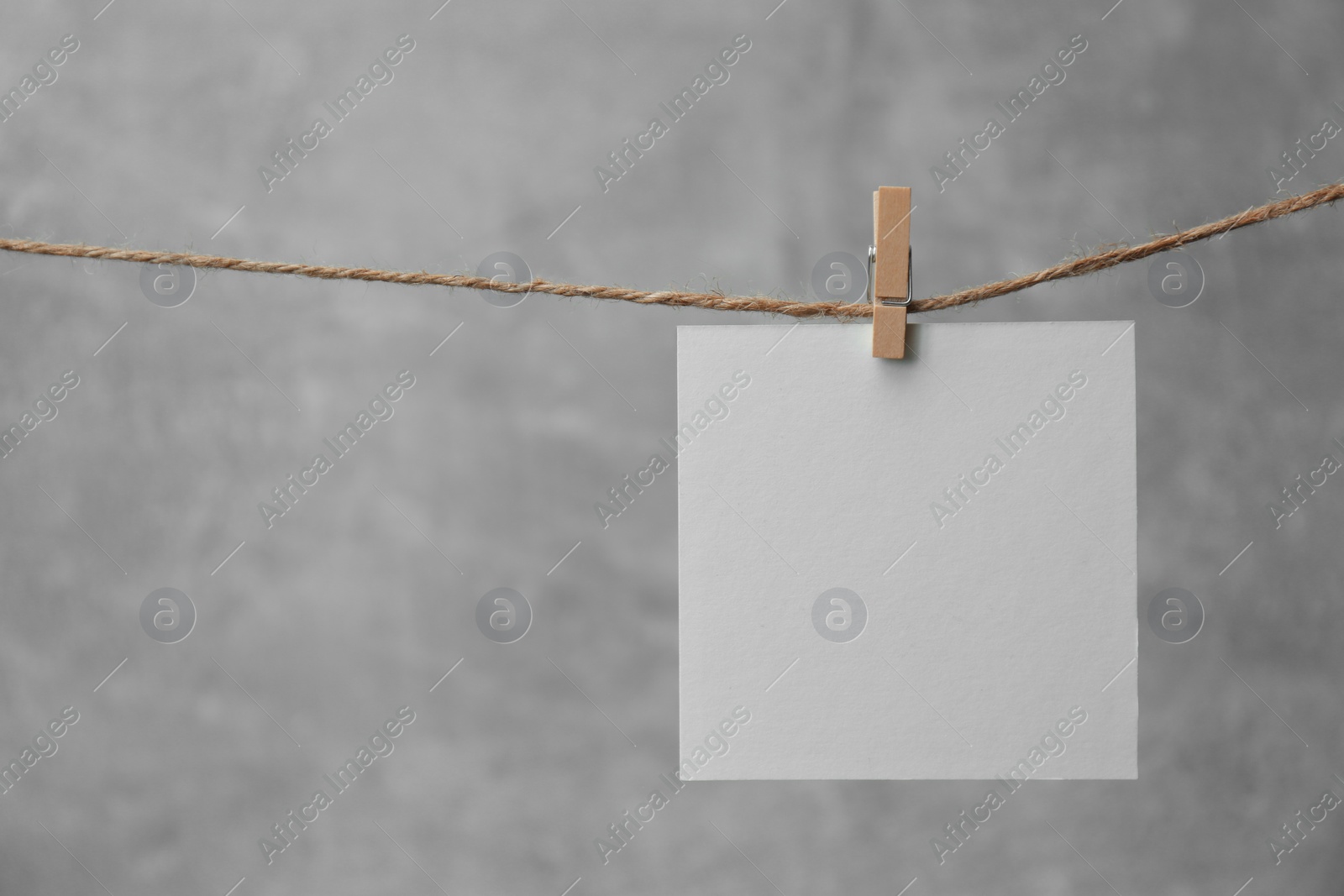 Photo of Wooden clothespin with blank notepaper on twine against grey background. Space for text