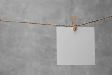 Photo of Wooden clothespin with blank notepaper on twine against grey background. Space for text