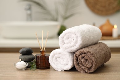 Photo of Spa composition. Rolled towels, aroma diffuser, massage stones and burning candle on wooden table indoors