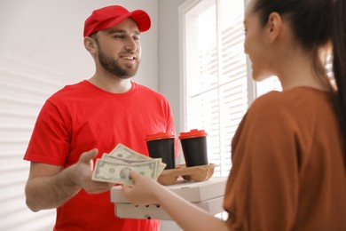 Photo of Young deliveryman receiving tips from woman indoors