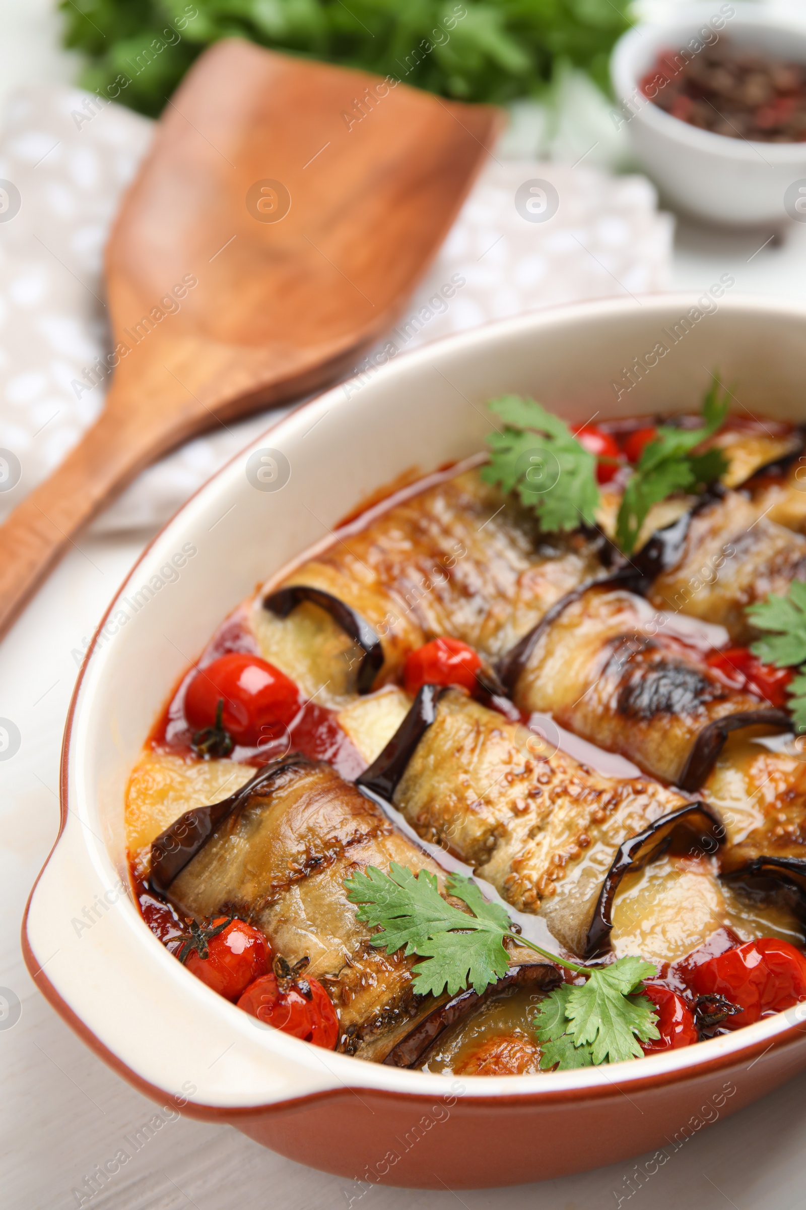 Photo of Tasty eggplant rolls with tomatoes, cheese and parsley in baking dish on white table, closeup