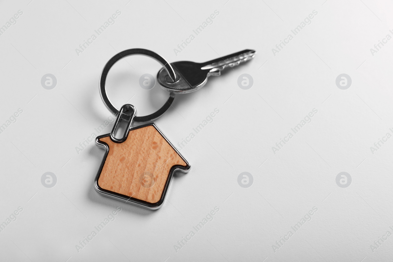 Photo of Key with trinket in shape of house on white background, above view and space for text. Real estate agent services