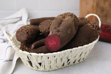 Whole and cut red beets in basket on light gray table, closeup