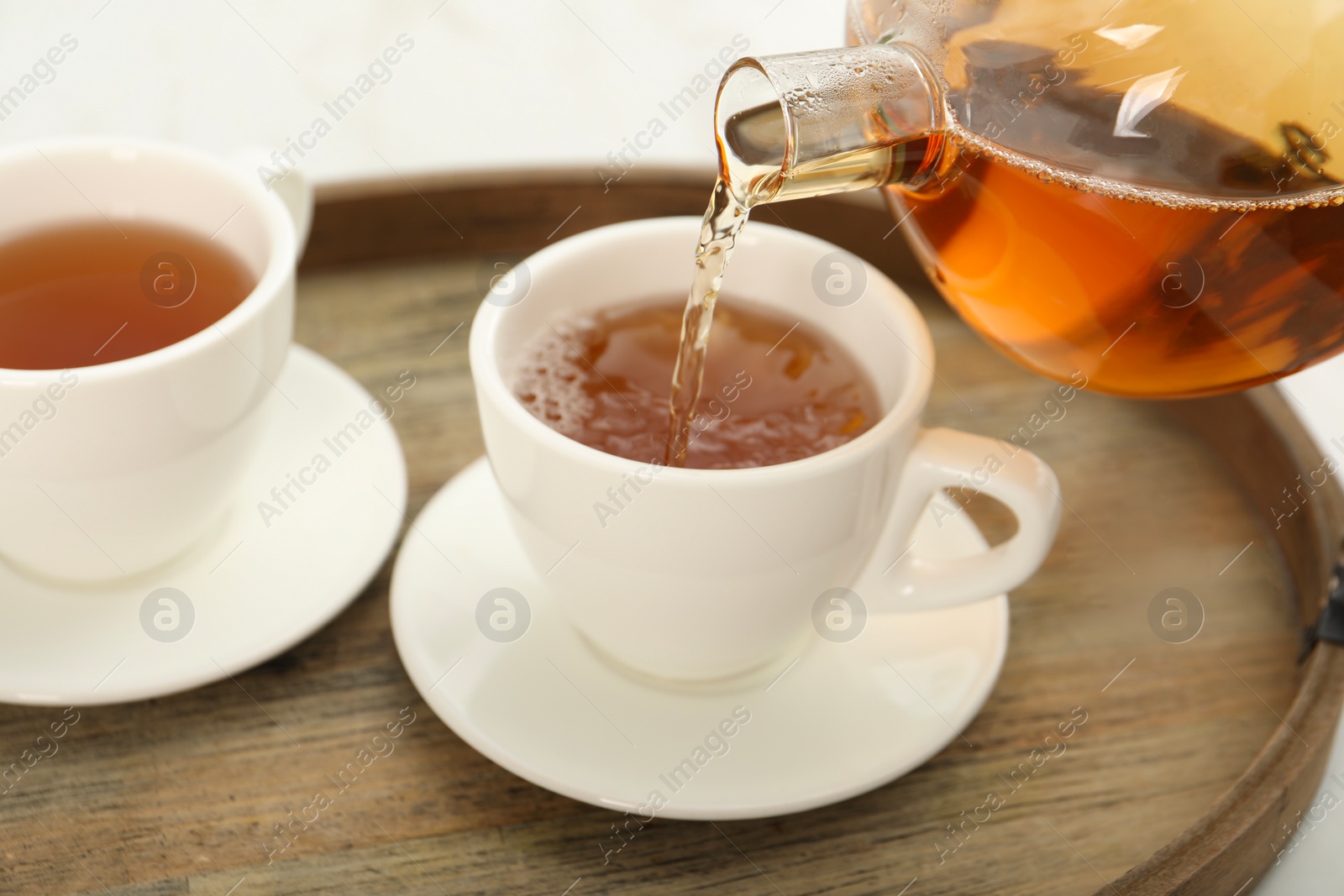 Photo of Pouring aromatic tea in cup at table, closeup