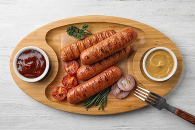 Photo of Delicious grilled sausages with sauces on wooden tray, top view. Barbecue food