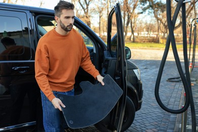 Photo of Man taking carpets from auto for cleaning at self-service car wash