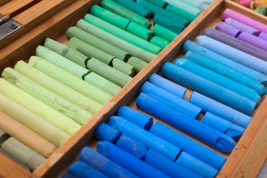 Photo of Set of soft pastels in wooden box as background, closeup. Drawing material