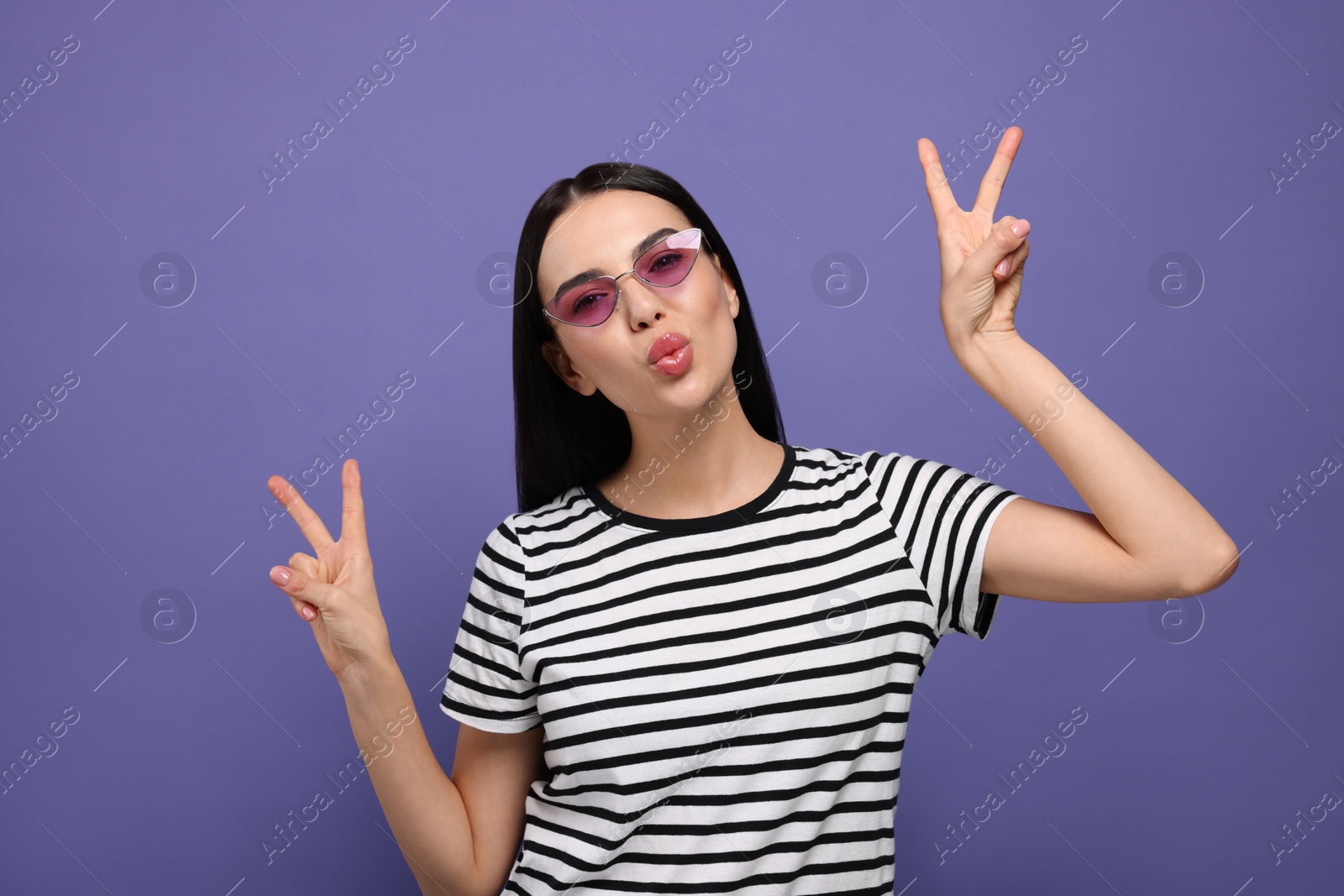 Photo of Beautiful young woman in stylish sunglasses blowing kiss on purple background