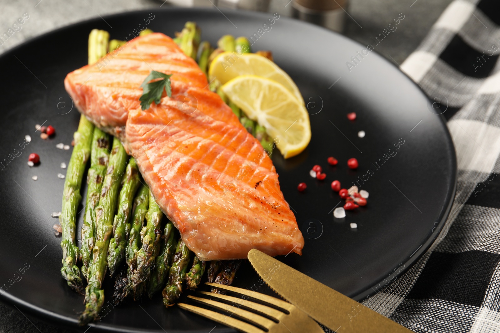 Photo of Tasty grilled salmon with asparagus, lemon and spices served on table, closeup