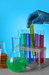 Photo of Scientist taking test tube with liquid at wooden table against light blue background, closeup