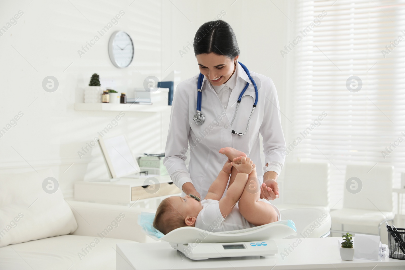 Photo of Young pediatrician weighting cute little baby in clinic