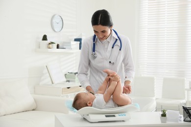 Photo of Young pediatrician weighting cute little baby in clinic