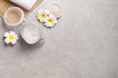 Photo of Body scrub, sea salt and plumeria flowers on grey table, flat lay. Space for text
