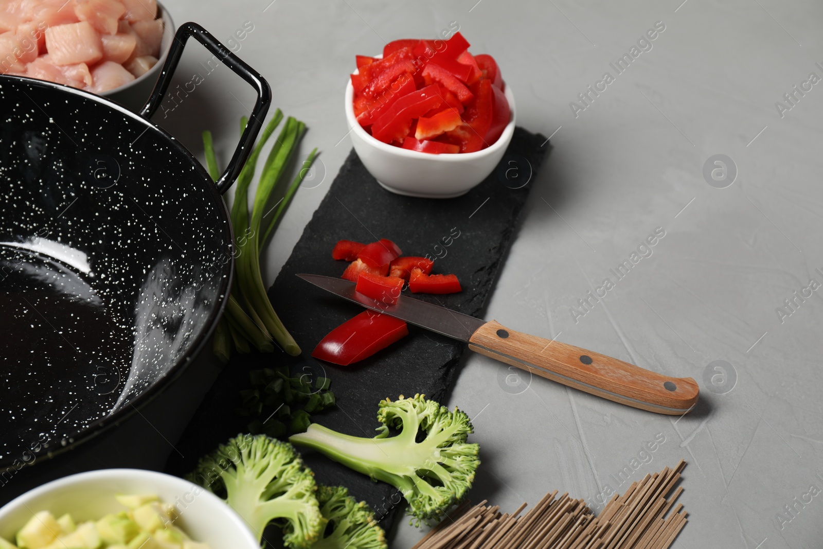 Photo of Wok pan, noodles, chicken and other products on light grey table