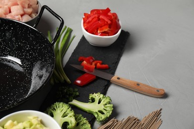 Wok pan, noodles, chicken and other products on light grey table