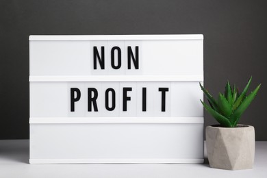 Photo of Lightbox with phrase Non Profit and houseplant on white table