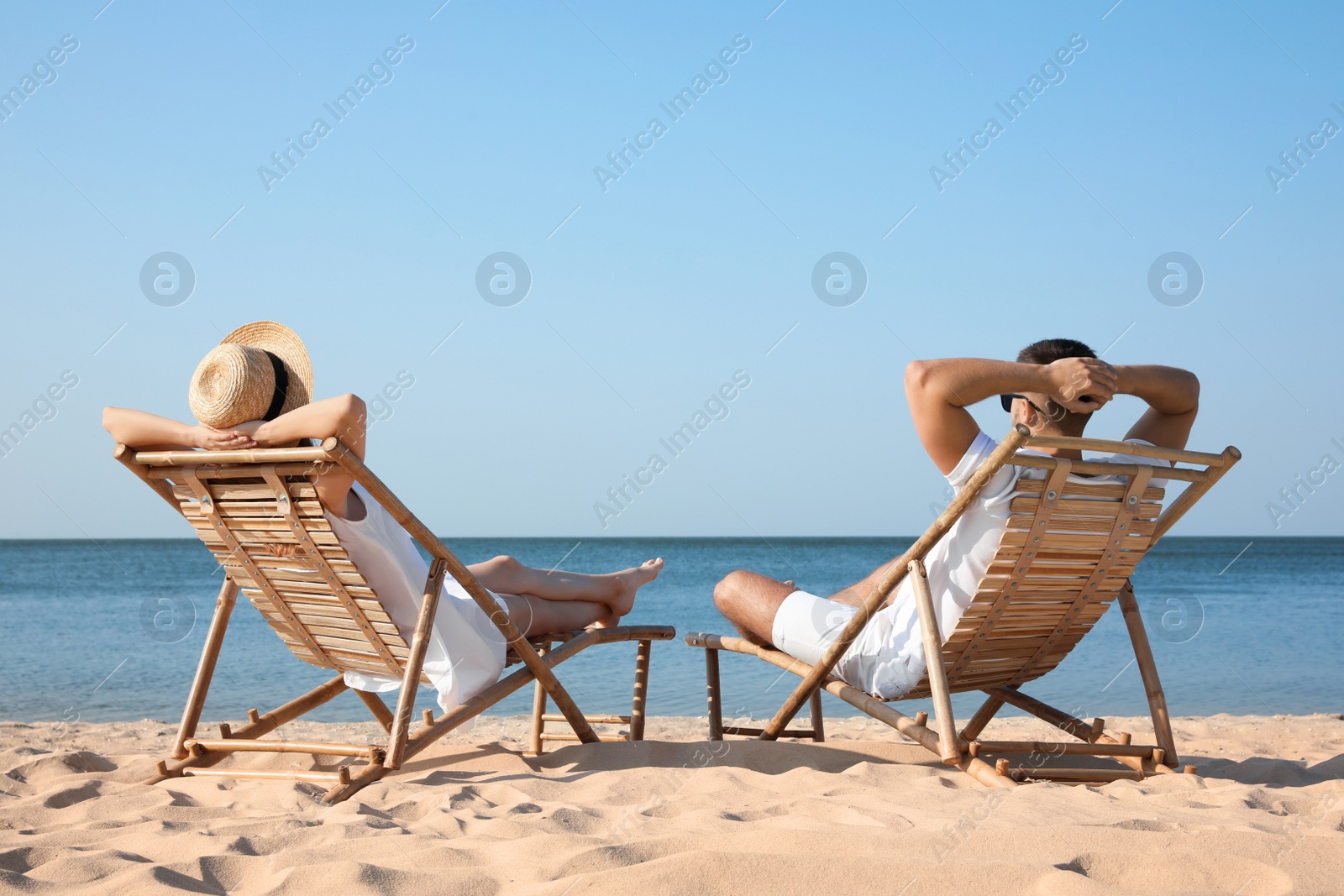 Photo of Young couple relaxing in deck chairs on beach