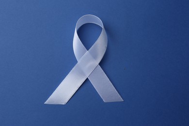 Photo of White awareness ribbon on blue background, top view