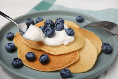 Putting natural yogurt onto tasty pancakes with blueberries at table, closeup