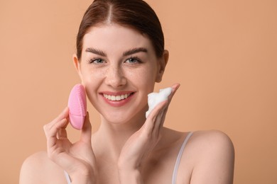 Photo of Washing face. Young woman with brush and cleansing foam on beige background